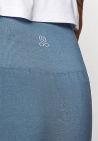 Blaue Leggings mit strukturiertem Finish, die ein kleines weißes Logo auf der Rückseite zeigen. Das Material wirkt dehnbar und enganliegend.