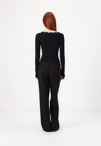 Long-sleeve black top with a scalloped lace neckline, paired with black wide-leg pants. Fabrics appear smooth and fitted at the waist.