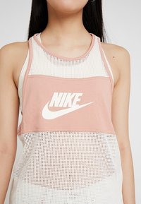 Nike ärmlös topp i ljusrosa och vitt, med meshdesign, logotyp tryckt på framsidan och avslappnad passform. Texturerad tyg framhäver stilen.