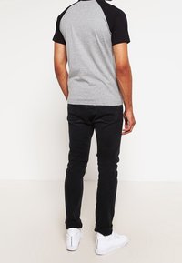 T-shirt raglan à manches courtes gris et noir, en mélange de coton, associé à un jean noir et des baskets blanches. Design simple, silhouette ajustée.