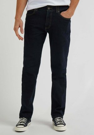 Jeans blu scuro in denim, con taglio dritto, design a cinque tasche e cuciture gialle. Abbinati a sneakers nere e bianche.