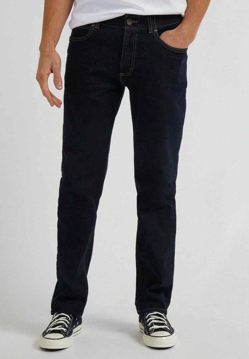 Jeans blu scuro in denim, con taglio dritto, design a cinque tasche e cuciture gialle. Abbinati a sneakers nere e bianche.