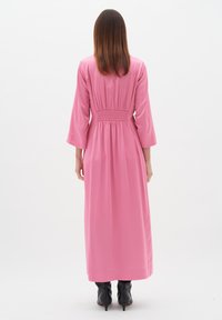 Rochie lungă roz, dintr-un material neted, cu talie elastică și mâneci trei sferturi, asortată cu cizme negre cu toc înalt.