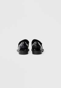 O pereche de pantofi eleganți din piele neagră lucioasă văzuți din spate pe un fundal simplu gri deschis.