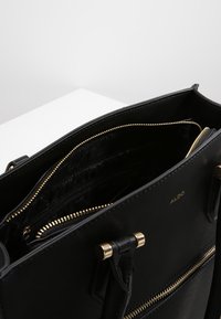 Czarna skórzana torebka z złotymi akcesoriami, z zamykanymi kieszeniami i gładką teksturą. Wnętrze zawiera wiele przegrod.