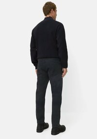 Zwarte trui met hoge hals, gecombineerd met donkere jeans. De outfit wordt afgemaakt met zwarte schoenen. Eenvoudig, minimalistisch ontwerp.