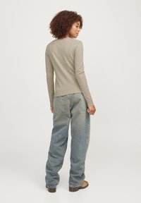 Helles beiges Langarmshirt mit figurbetontem Design. Kombiniert mit lockeren, ausgeblichenen blauen Jeans mit hoher Taille und aufgesetzten Taschen.