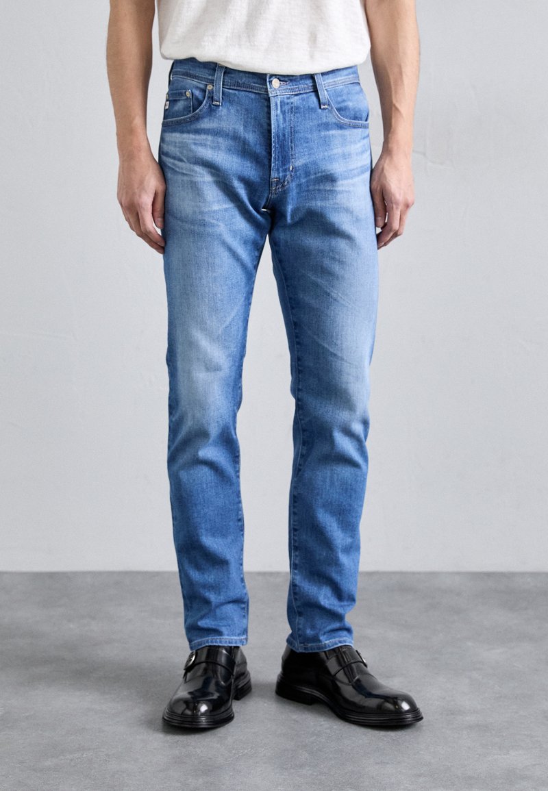 Svetlo modré džínsy s rovný strihom, piatimi vreckami, jemným vyblednutím a gombíkovým zapínaním, skombinované s čiernymi lesklými topánkami.