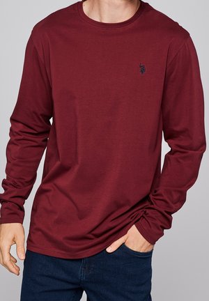 Bordeauxrotes Langarm-T-Shirt aus Baumwolle mit Rundhalsausschnitt und kleinem, gesticktem Logo auf der Brust. Glatte Textur und entspannte Passform.