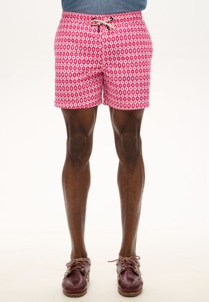 Bañador rosa con un patrón geométrico en blanco, con cinturilla elástica y cordón. Combinado con zapatos náuticos marrones.