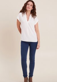 Blouse blanche à manches courtes avec un décolleté en V, assortie à un jean ajusté bleu marine et des bottines brunes. Tissu lisse avec des détails de texture subtils.