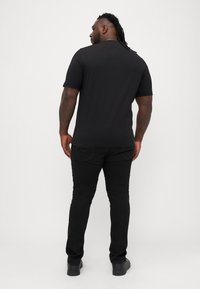 Must t-särk lühikeste varrukatega, sile puuvillane kangas, lõdva lõikega, tagantvaade, koos mustade teksade ja mugavate mustade jalatsitega.