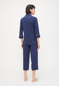 Conjunto de pijama riscado em azul marinho, com mangas três quartos e calças cropped. Apresenta riscas brancas e um colarinho recortado. Tecido suave ao toque.