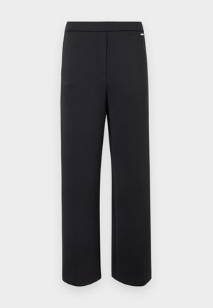 Pantalon noir droit avec une fermeture frontale dissimulée et un petit logo métallique près de la ceinture sur fond blanc.