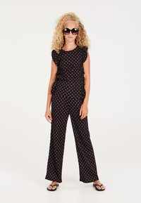 Tuta nera con maniche a sbuffo e motivo floreale rosso. Design a gamba larga abbinato a infradito nere e occhiali da sole oversized.