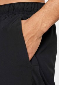 Pantalones cortos deportivos negros con un bolsillo de malla y una cinturilla elástica. La textura es suave; el material parece ligero y transpirable.