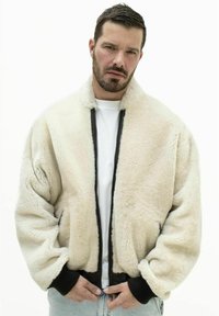Creme faux fur bomberjakke med lynlås i sort, ribbede manchetter og høj krave. Bæres over en hvid t-shirt med en afslappet pasform.