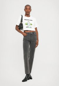 Bela skrajno skrajšana majica s grafiko in napisom "Moschino Jeans". Sive ravne hlače. Črna torbica in gležnjarji s srebrnimi dodatki.