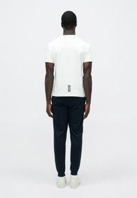 Fehér pamut rövid ujjú póló, hátul vízszintes csíkokkal. Sötétkék nadrággal és fehér tornacipővel párosítva.