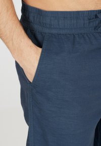 Marina blå shorts i ett lättviktsmaterial, med elastisk midja och sidofickor. Slät textur med subtil lyster.