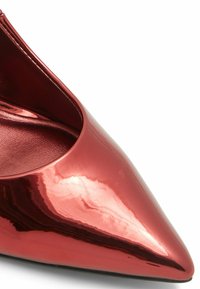 Červená lakovaná stiletto bota s špičatou špičkou a elegantním designem. Lesklý povrch odráží světlo a zvyšuje její hladkou texturu.