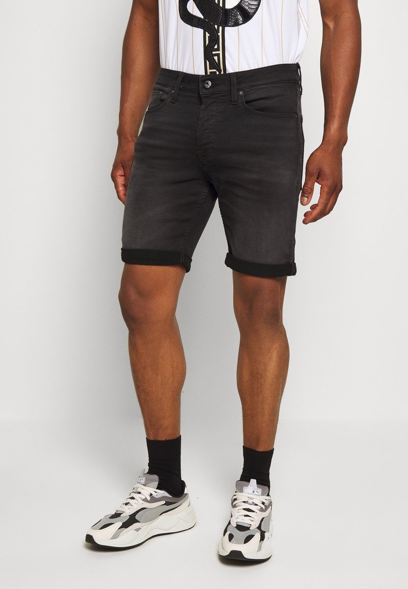 Pantaloni corti in denim nero con risvolti, caratterizzati da un design slim fit e una lieve scoloritura. Abbinate a sneaker bianche e grigie.