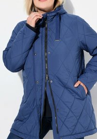 Chaqueta acolchada azul con capucha, que presenta un cierre frontal con cremallera, cierres de broche y bolsillos laterales. Fabricada con un material suave y acolchado.