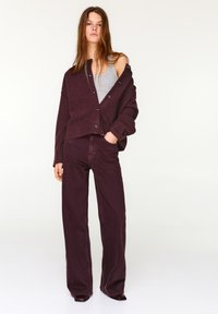 Bordó, túlméretezett kardigán V-nyakkivágással és gombokkal, szürke trikóval és bordó, bő szárú nadrággal párosítva. Simított textúra, kényelmes szabás.