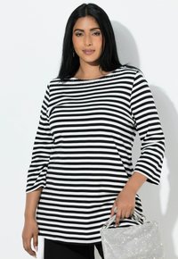 Czarnobiała bluzka w paski z rękawami o długości do łokcia, okrągłym dekoltem i ozdobami przy kołnierzu. Połączona ze srebrną torebką.