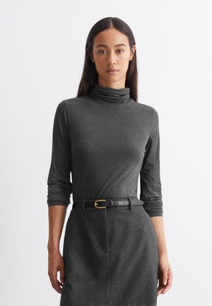 Grauer Rollkragenpullover mit langen Ärmeln, figurbetontem Schnitt, weichem Material, kombiniert mit einem Rock mit hoher Taille und einem schwarzen Gürtel mit goldener Hardware.