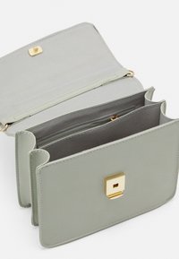 Světle zelená kožená kabelka se zlatým čtvercovým zapínáním, která má více přihrádek a texturovaný interiér. Zobrazený otevřený pohled.