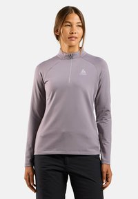 Hellblaues Langarm-Zip-Up-Oberteil mit Stehkragen, das ein Logo auf der Brust hat und aus glattem, dehnbarem Material besteht. Kombiniere es mit dunklen Hosen.