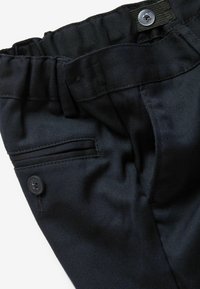 Pantalons noirs avec une taille élastique, poches latérales avec rabat et détail de bouton à l'avant. Le matériau a une texture lisse et tissée.