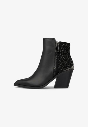 Stivaletto nero alla caviglia con punta affusolata, realizzato in pelle liscia e tessuto testurizzato. Dotato di una cerniera laterale e di borchie decorative sul retro.