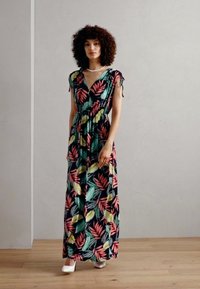 Abito lungo in tessuto elastico con uno sfondo scuro e vivaci motivi di foglie tropicali in verde, rosa e giallo. Collo a V e vita arricciata.