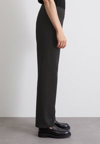 Slim-fit, tummanharmaat venyvät housut, joissa on korkea vyötärö, sivutaskut ja sileä pinta, yhdistettynä mustiin, paksupohjaisiin kenkiin.