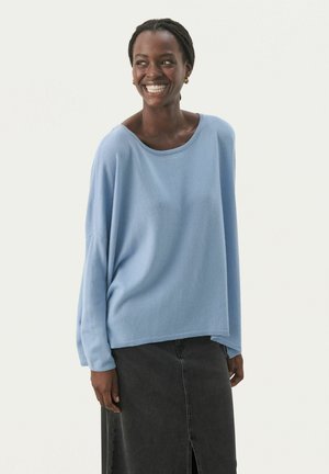 Pull léger bleu, ample, avec un col large et des poignets côtelés, assorti à une jupe en denim foncé longue avec une fente à l'avant.