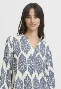 Langarmshirt in Creme mit einem blauen, kunstvollen Paisleymuster, V-Ausschnitt und weichem, strukturiertem Stoff.