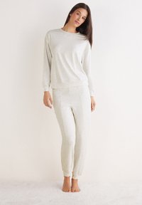 Lichtgrijze loungewearset met lange mouwen en jogger-stijl broek, gemaakt van zachte, gestructureerde stof, met subtiele stikdetails.
