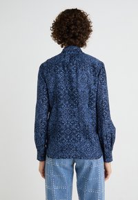 Camicia a maniche lunghe in tessuto blu scuro con un dettagliato motivo floreale e geometrico blu chiaro, dotata di colletto classico e polsini abbottonati.