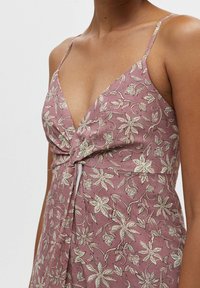 Helles lila Kleid mit floralem Muster, V-Ausschnitt, dünnen Trägern und einem gedrehten Knotendetail an der Taille. Hergestellt aus strukturiertem Stoff.