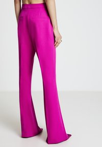 Fuchsiaweite Hosen mit weitem Bein aus glattem Stoff, mit Gesäßtaschen und einer maßgeschneiderten hohen Taille, die eine klare, moderne Silhouette zeigt.