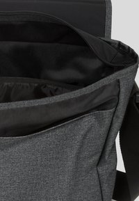 Borsa messenger in tessuto grigio con una grande tasca interna nera e una superficie liscia. Presenta una chiusura a patta e una tracolla regolabile.