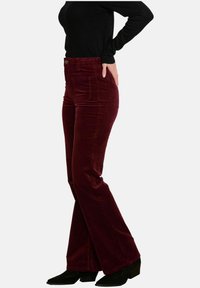 Pantalones de pana burdeos de corte acampanado con cintura alta, bolsillos laterales y una superficie texturizada. Combinados con una blusa de manga larga negra y botas negras.