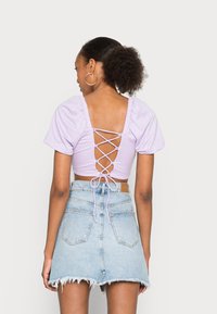 Top lilás cropped com mangas bufantes e costas entrelaçadas com cordas. Combinado com uma saia mini de jeans clara de cintura alta com bainha desfiada.