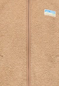 Beige fleecejakke med teksturert overflate, hel glidelås og en liten fargerik merkeetikett på venstre side.