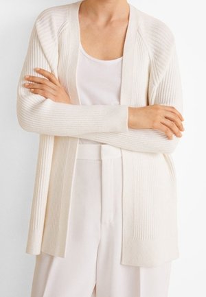 Ivore geribde cardigan met een open voorkant, lange mouwen en een gestructureerde stof. Draagt over een witte tanktop en lichte broek.