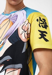 Camiseta gráfica que presenta una mezcla de colores azul, amarillo y negro. El diseño muestra arte de personajes estilizados con contornos marcados y caracteres japoneses.
