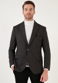 Tumehall blazer tekstuuriga mustriga, kahe esipocketiga, ühe nööbiga kinnitamine ja kontrastses valges kõrge kaelusega pluus all.