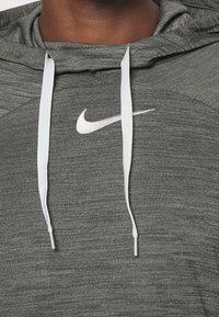 Hoodie gris avec un tissu texturé, des cordons blancs et un logo Nike blanc sur la poitrine.